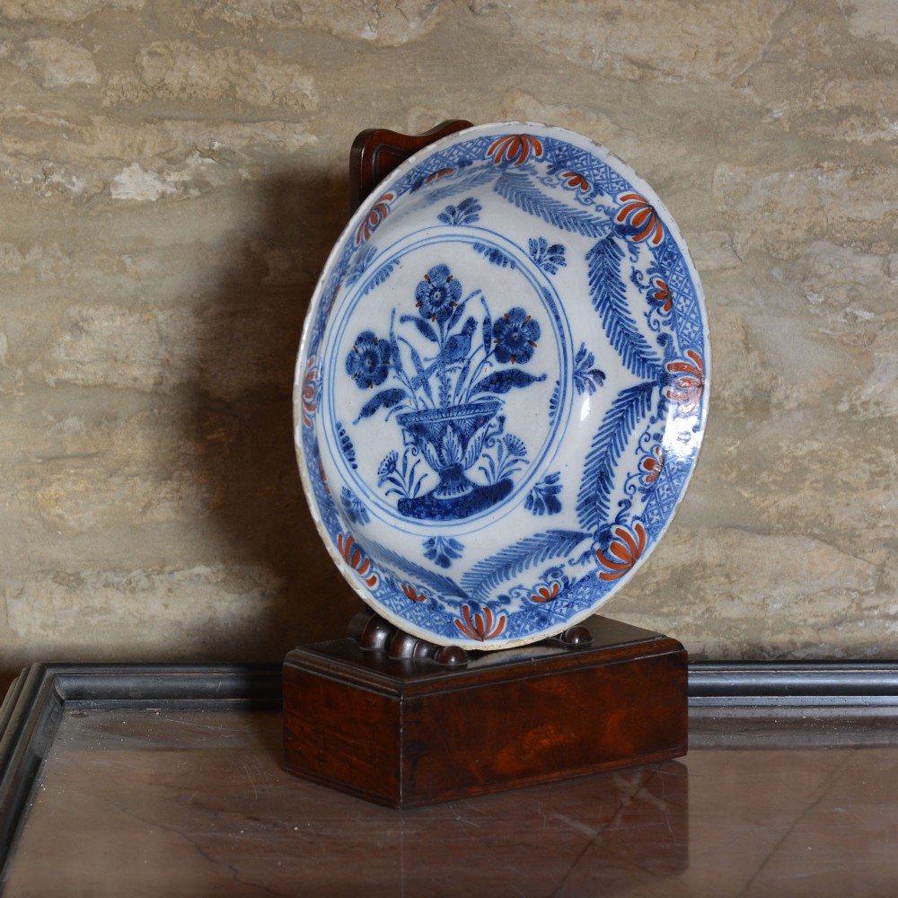 A circular 18th-century tin-glazed Delftware shallow bowl featuring hand-painted cobalt blue floral motifs and iron-red accents. View II