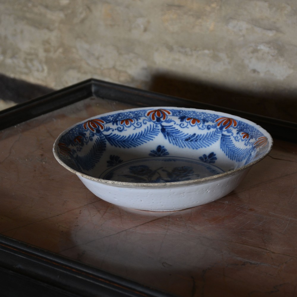 A circular 18th-century tin-glazed Delftware shallow bowl featuring hand-painted cobalt blue floral motifs and iron-red accents. View IV