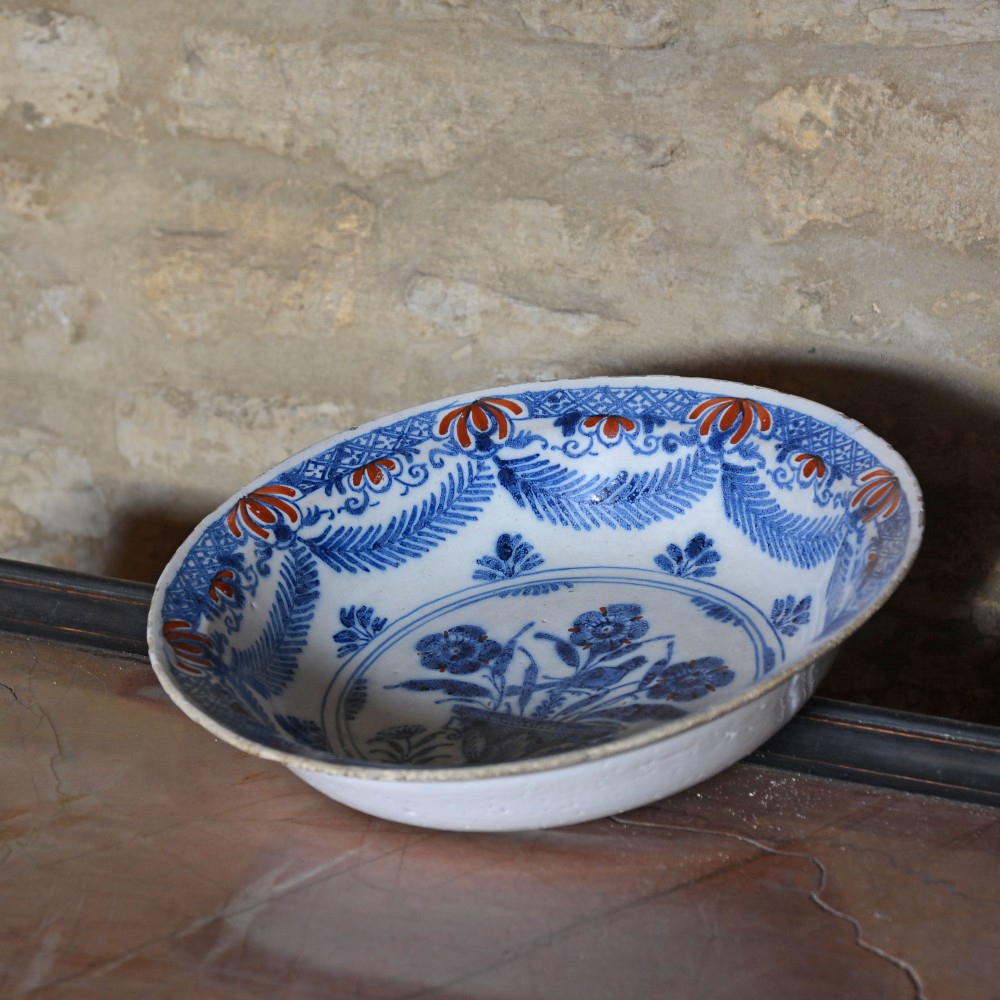 A circular 18th-century tin-glazed Delftware shallow bowl featuring hand-painted cobalt blue floral motifs and iron-red accents. View V