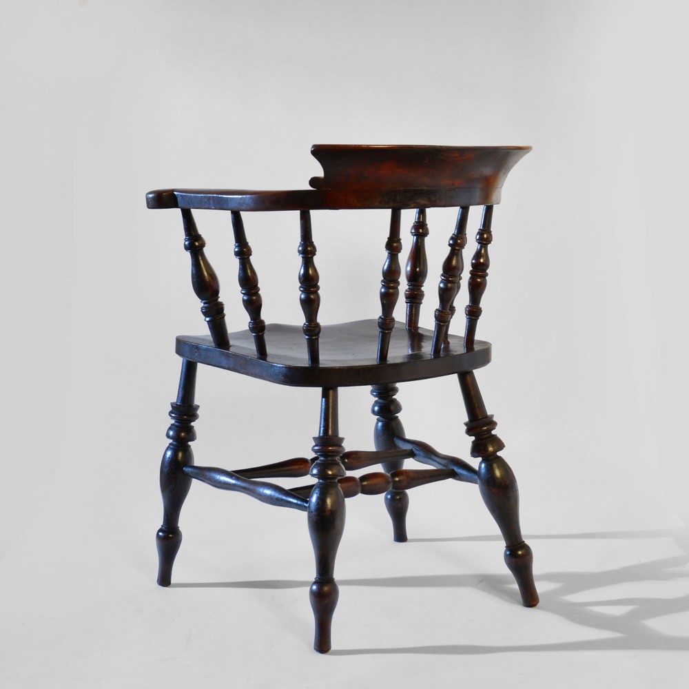A nineteenth-century dark-stained ash and elm Windsor armchair featuring turned spindles, a curved arm rail, a saddle seat, and turned legs with stretchers. View II