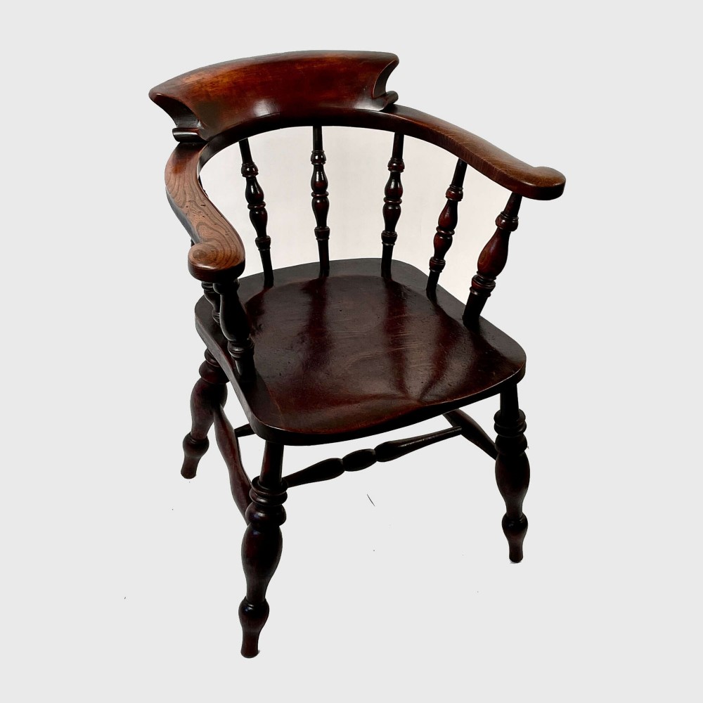 A nineteenth-century dark-stained ash and elm Windsor armchair featuring turned spindles, a curved arm rail, a saddle seat, and turned legs with stretchers. View IV