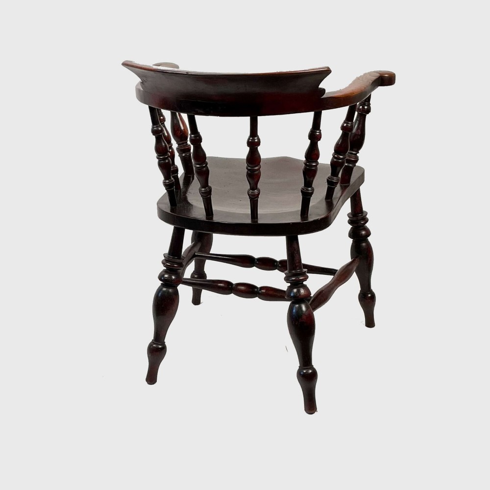 A nineteenth-century dark-stained ash and elm Windsor armchair featuring turned spindles, a curved arm rail, a saddle seat, and turned legs with stretchers. View V