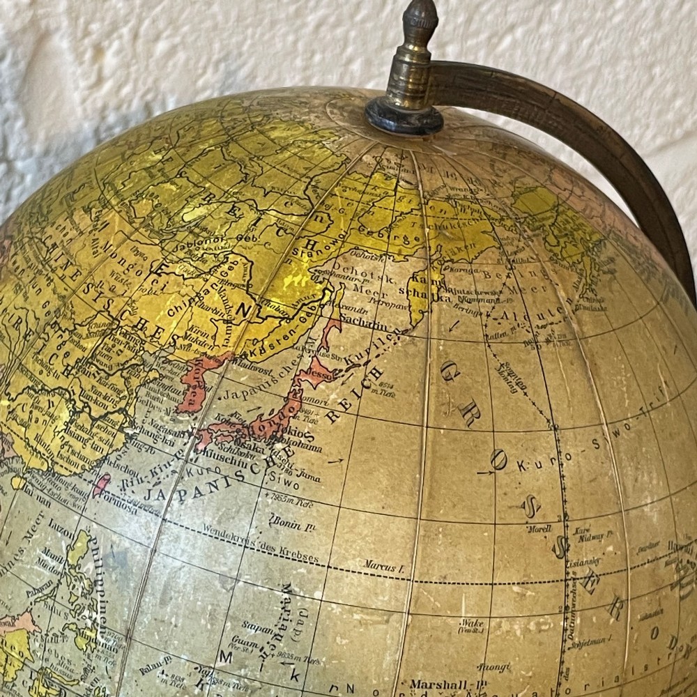 An early 20th-century German terrestrial desk globe featuring printed paper map gores, a graduated brass meridian ring, and a turned ebonised wooden base. View V