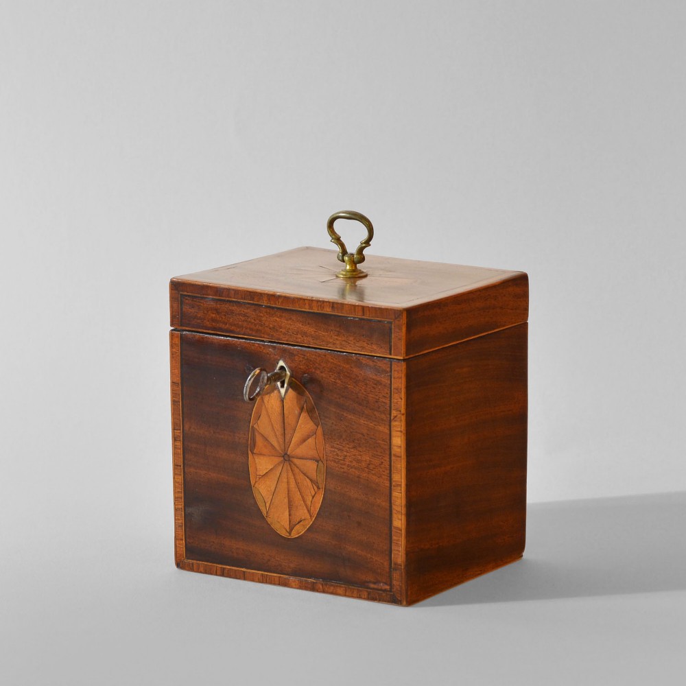 An 18th-century Sheraton mahogany square tea caddy with a top brass handle, key in lock, and an oval inlaid shell motif on the front.