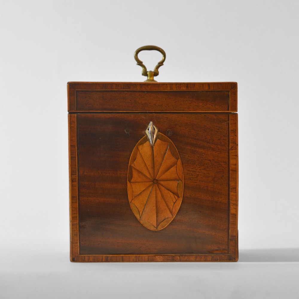 An 18th-century Sheraton mahogany square tea caddy with a top brass handle, key in lock, and an oval inlaid shell motif on the front. View II