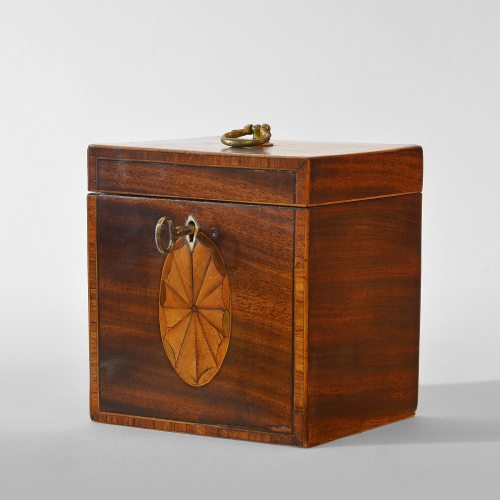 An 18th-century Sheraton mahogany square tea caddy with a top brass handle, key in lock, and an oval inlaid shell motif on the front. View IV