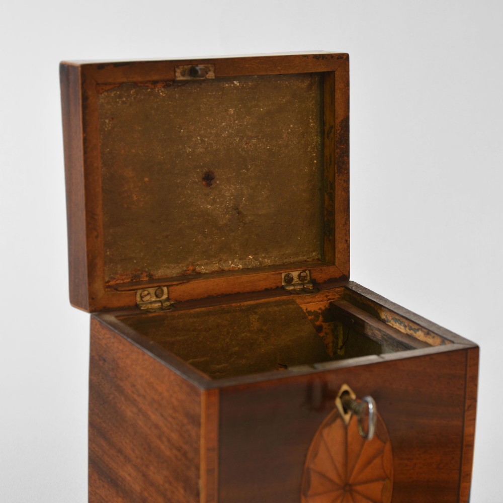 An 18th-century Sheraton mahogany square tea caddy with a top brass handle, key in lock, and an oval inlaid shell motif on the front. View V