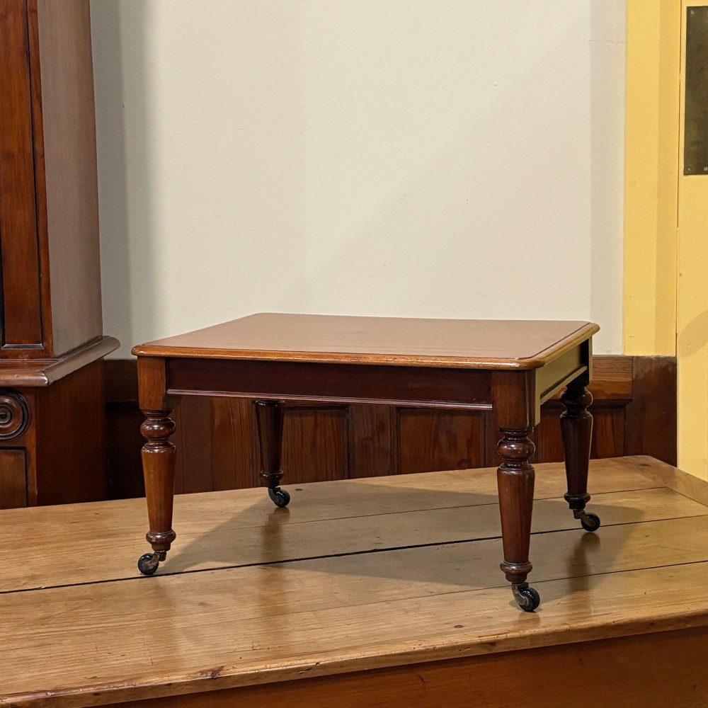 A rectangular miniature mahogany table featuring turned legs fitted with brass castors and a polished top. View II