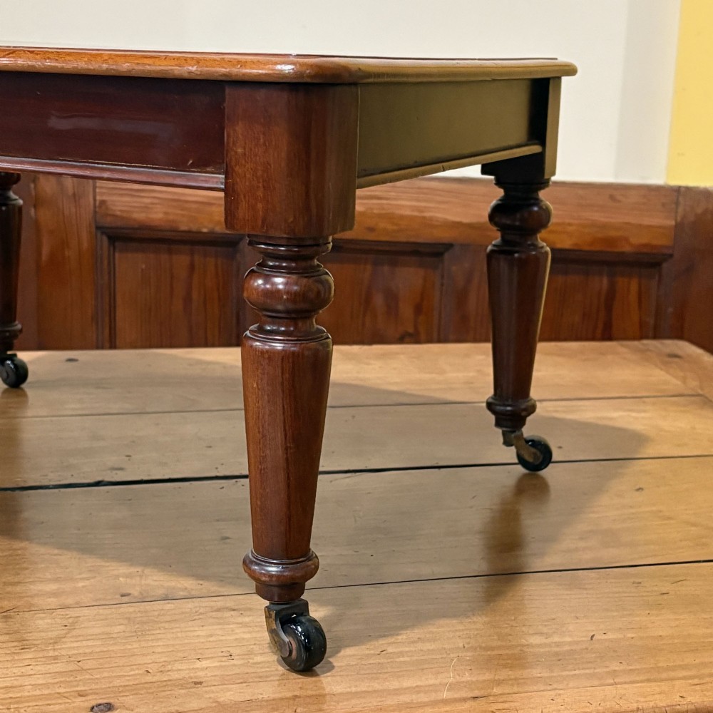 A rectangular miniature mahogany table featuring turned legs fitted with brass castors and a polished top. View III