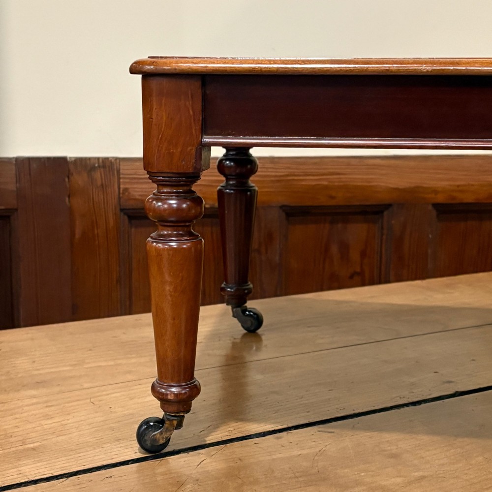 A rectangular miniature mahogany table featuring turned legs fitted with brass castors and a polished top. View IV