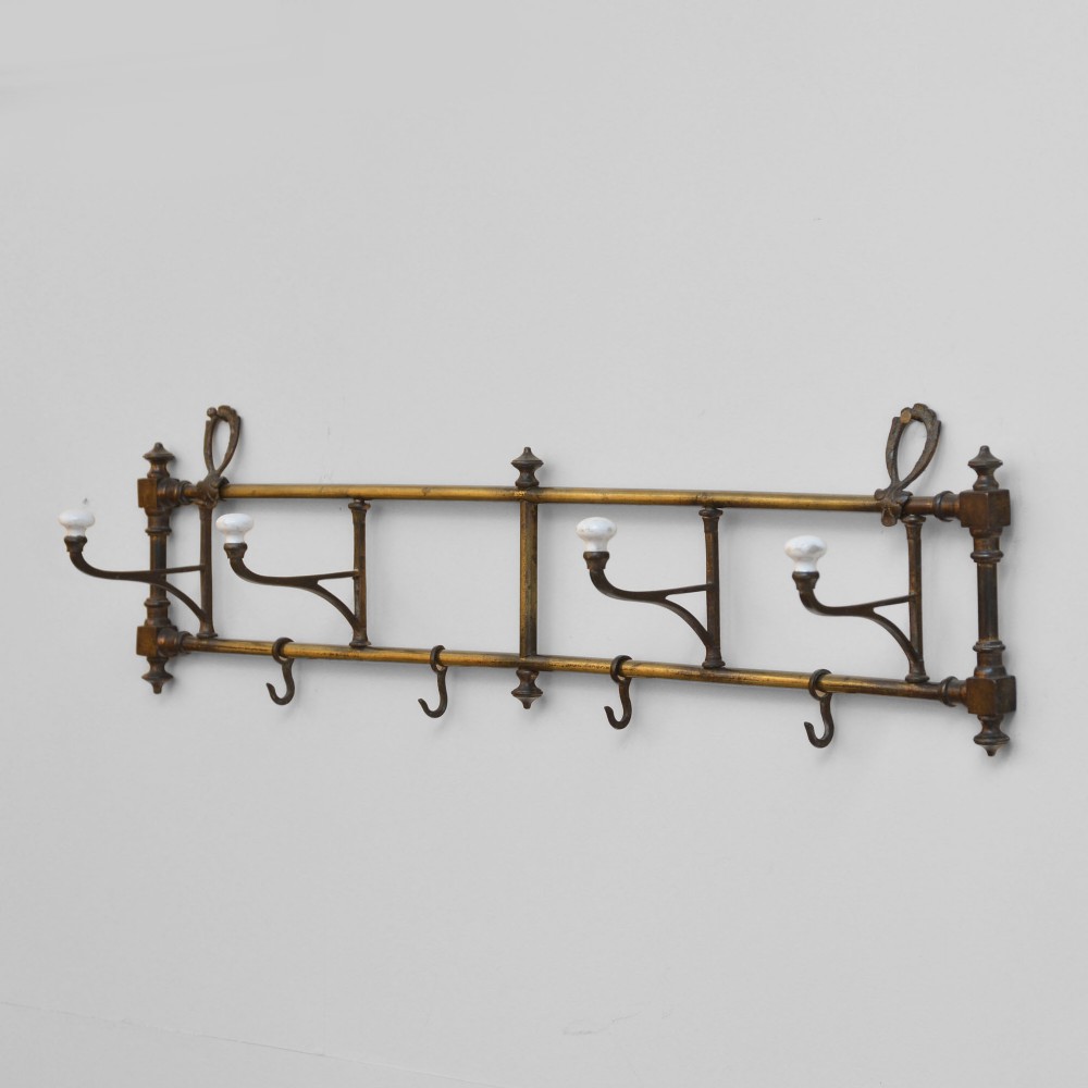 A wall-mounted aged brass coat rack featuring two horizontal bars, four ceramic-tipped upper hooks, and four hanging lower hooks.
