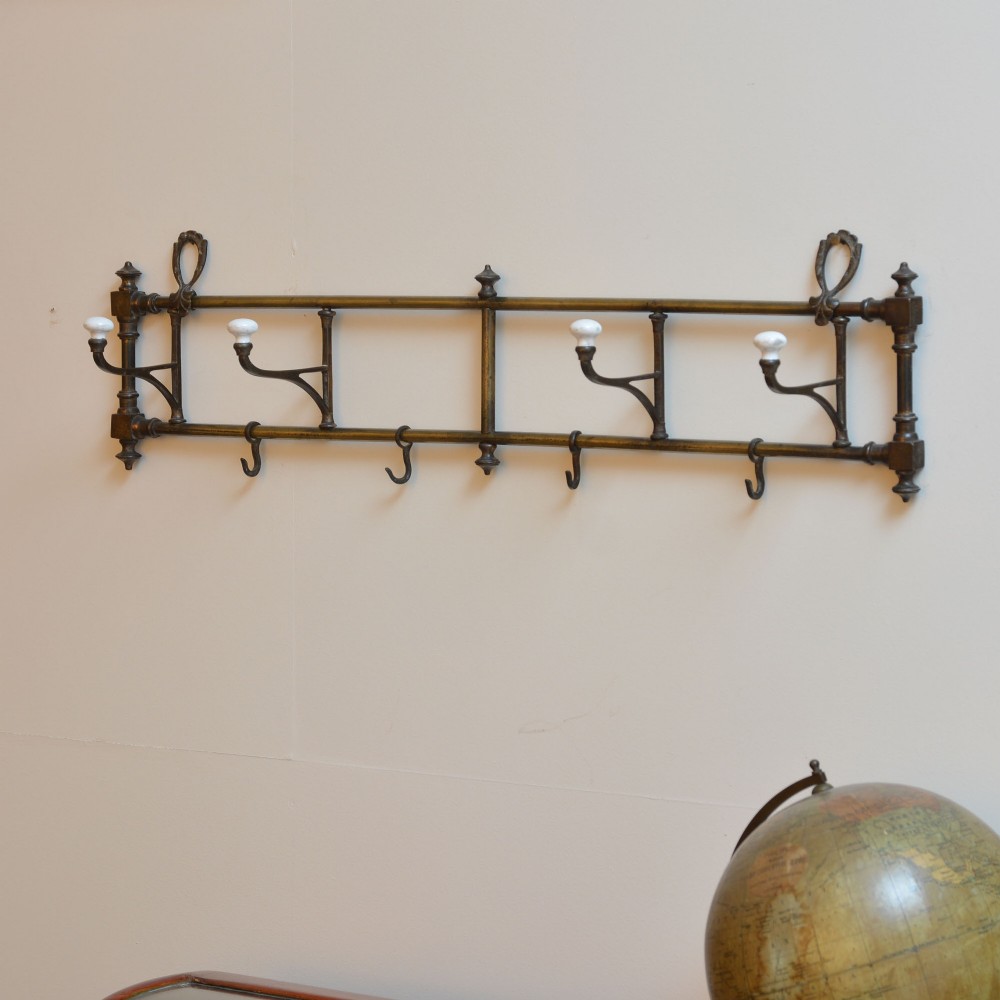 A wall-mounted aged brass coat rack featuring two horizontal bars, four ceramic-tipped upper hooks, and four hanging lower hooks. View III