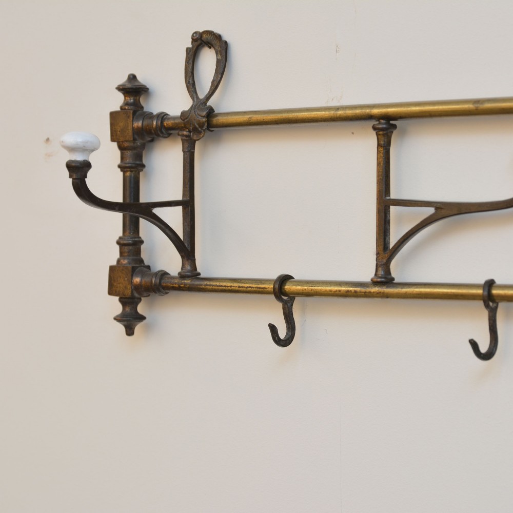 A wall-mounted aged brass coat rack featuring two horizontal bars, four ceramic-tipped upper hooks, and four hanging lower hooks. View IV