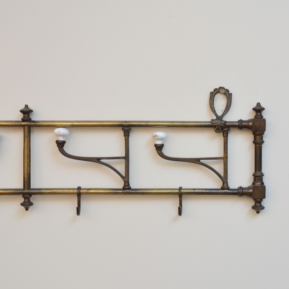 A wall-mounted aged brass coat rack featuring two horizontal bars, four ceramic-tipped upper hooks, and four hanging lower hooks. View V
