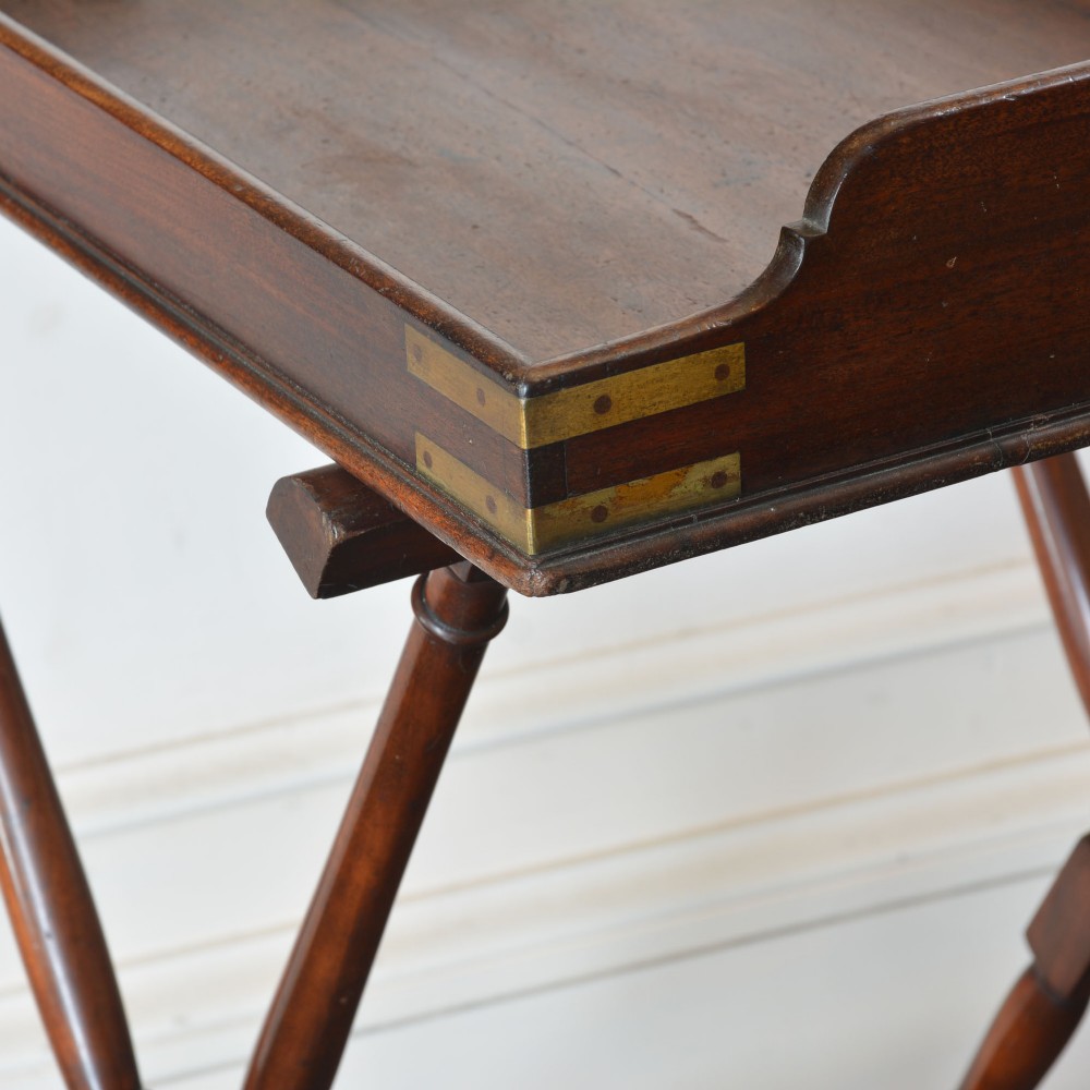 An antique dark mahogany butler tray with gallery edges and brass corner brackets set atop a folding x-frame stand with turned wooden legs. View III