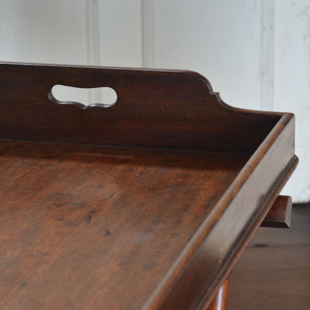 An antique dark mahogany butler tray with gallery edges and brass corner brackets set atop a folding x-frame stand with turned wooden legs. View IV