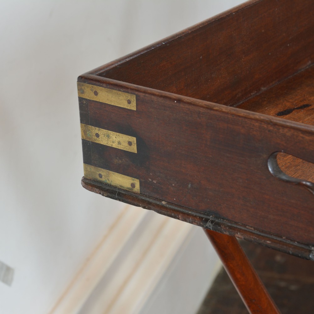 An antique dark mahogany butler tray with gallery edges and brass corner brackets set atop a folding x-frame stand with turned wooden legs. View V