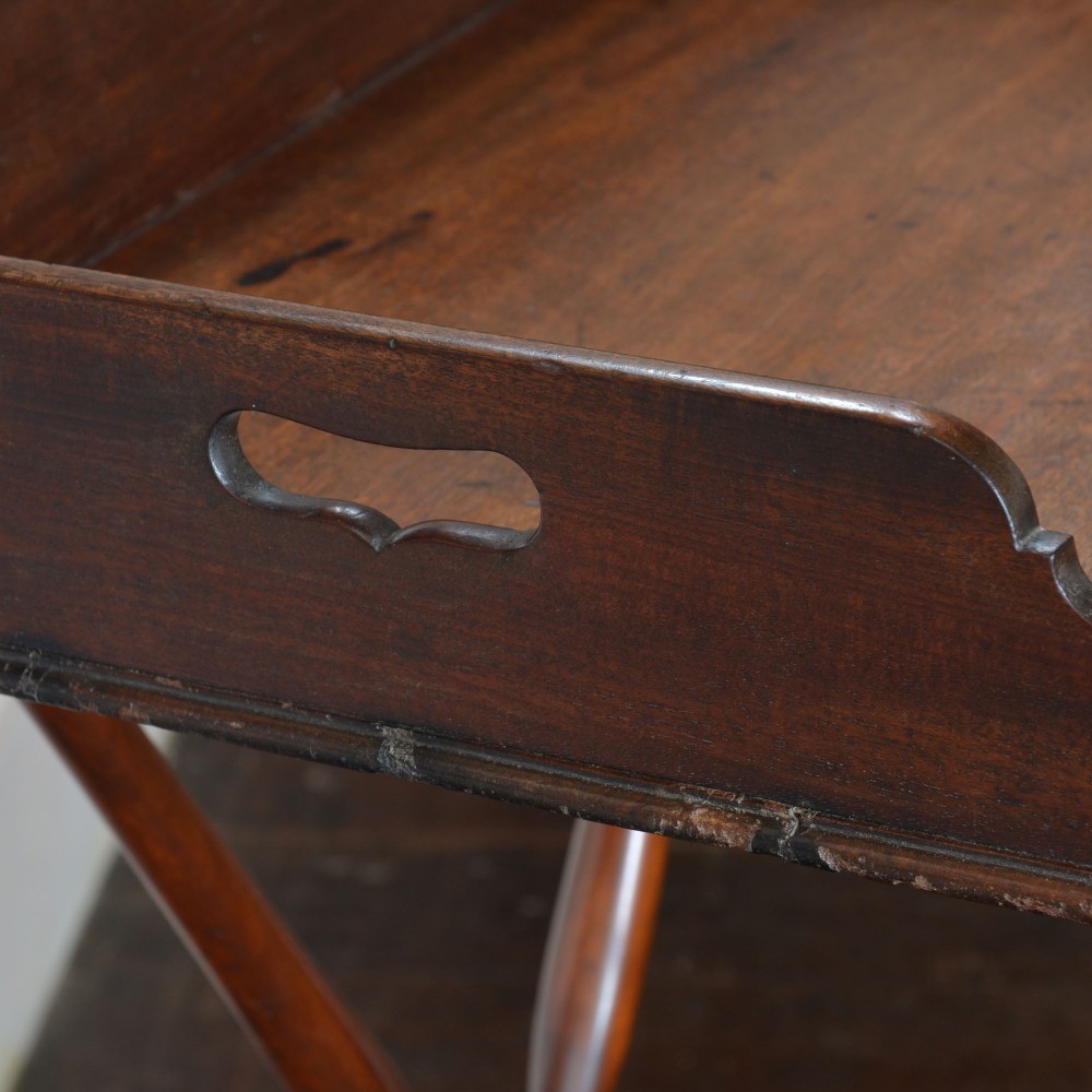 An antique dark mahogany butler tray with gallery edges and brass corner brackets set atop a folding x-frame stand with turned wooden legs. View VI
