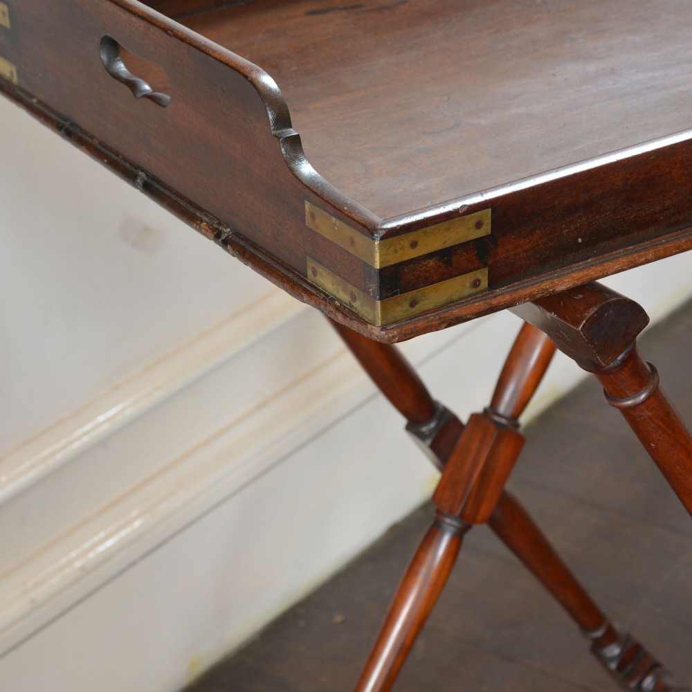 An antique dark mahogany butler tray with gallery edges and brass corner brackets set atop a folding x-frame stand with turned wooden legs. View VII