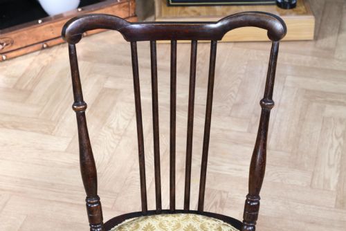 fig 3. An Edwardian dark walnut nursing chair featuring a spindled stick back, turned legs, and a patterned yellow fabric seat.