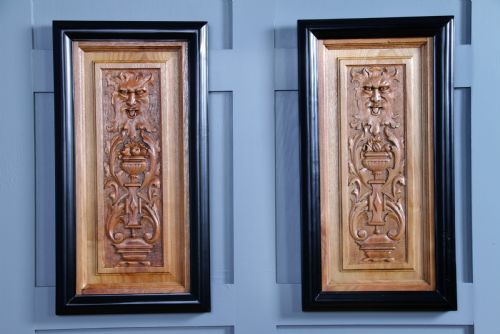 fig 1. A pair of rectangular carved walnut wall panels featuring detailed grotesque masks and classical urns set within black ebonised frames.