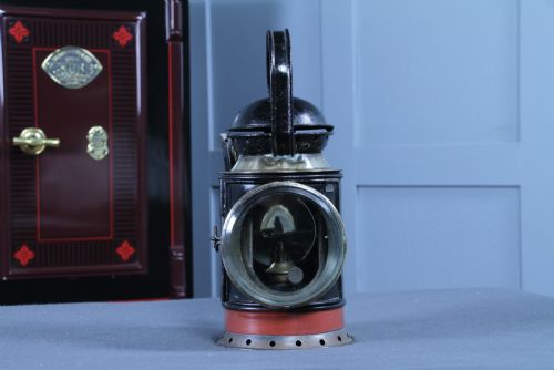 fig 1. An antique black painted iron GWR railway hand lantern featuring a circular glass lens, top handle, brass accents, and a red painted band near the base.
