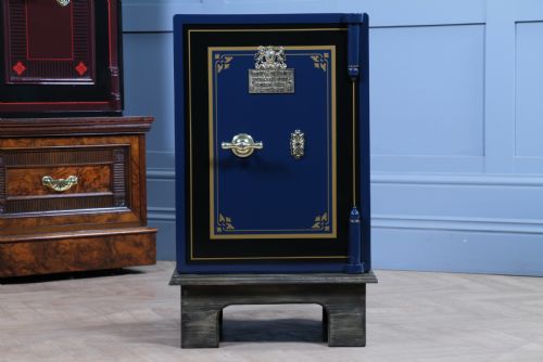 fig 2. A restored Victorian navy blue and black cast iron safe featuring polished brass hardware and a makers plaque, raised on a dark wooden plinth.