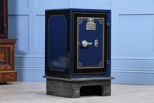 fig 3. A restored Victorian navy blue and black cast iron safe featuring polished brass hardware and a makers plaque, raised on a dark wooden plinth.