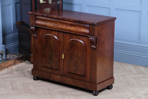 fig 1. A Victorian flame mahogany two-door sideboard featuring a cushion drawer, arched panel doors, carved corbels, and turned bun feet.