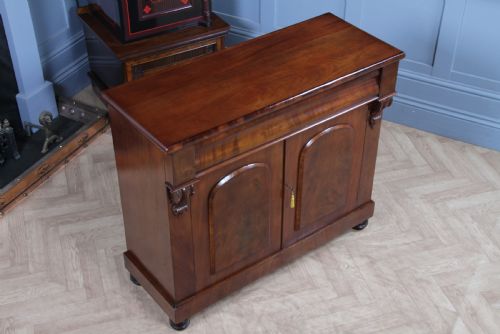 fig 2. A Victorian flame mahogany two-door sideboard featuring a cushion drawer, arched panel doors, carved corbels, and turned bun feet.
