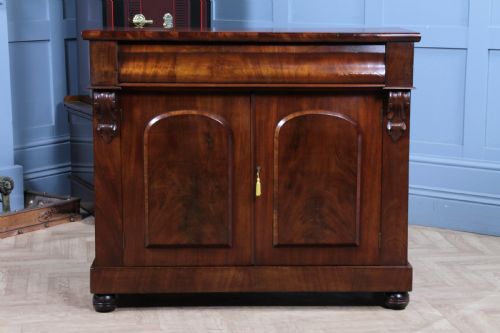 fig 3. A Victorian flame mahogany two-door sideboard featuring a cushion drawer, arched panel doors, carved corbels, and turned bun feet.