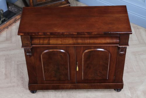 fig 4. A Victorian flame mahogany two-door sideboard featuring a cushion drawer, arched panel doors, carved corbels, and turned bun feet.