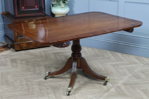 fig 2. A Regency mahogany tilt-top dining table featuring a rectangular crossbanded top supported by a turned pedestal column and four reeded sabre legs with brass castors.