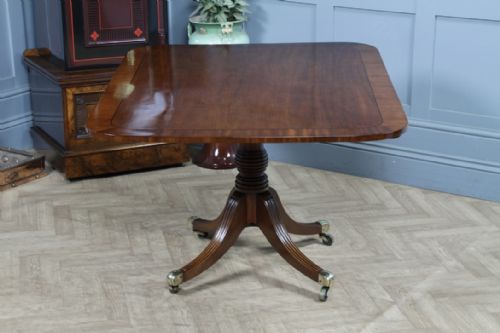 fig 3. A Regency mahogany tilt-top dining table featuring a rectangular crossbanded top supported by a turned pedestal column and four reeded sabre legs with brass castors.