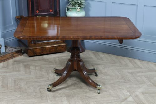 fig 4. A Regency mahogany tilt-top dining table featuring a rectangular crossbanded top supported by a turned pedestal column and four reeded sabre legs with brass castors.