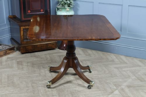 fig 5. A Regency mahogany tilt-top dining table featuring a rectangular crossbanded top supported by a turned pedestal column and four reeded sabre legs with brass castors.