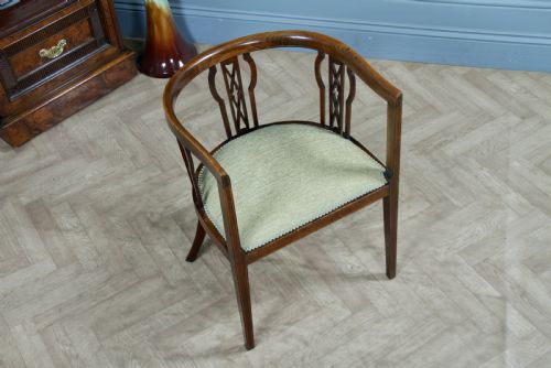 fig 2. An Edwardian inlaid mahogany tub armchair featuring a continuous curved backrest, pierced splats, and a sage green upholstered seat.