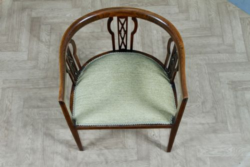 fig 3. An Edwardian inlaid mahogany tub armchair featuring a continuous curved backrest, pierced splats, and a sage green upholstered seat.