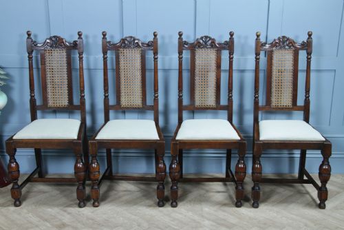 fig 2. A set of four dark oak Jacobean Revival dining chairs featuring woven cane backs, carved crests, turned legs, and cream fabric seats.