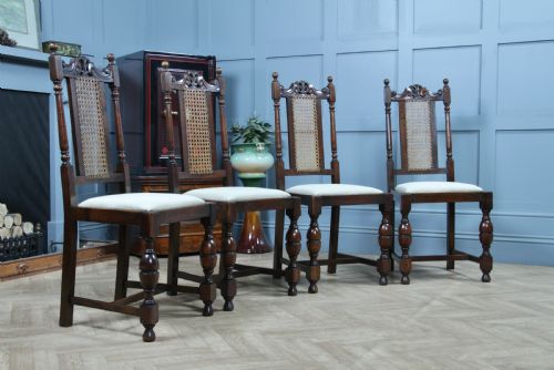 fig 3. A set of four dark oak Jacobean Revival dining chairs featuring woven cane backs, carved crests, turned legs, and cream fabric seats.