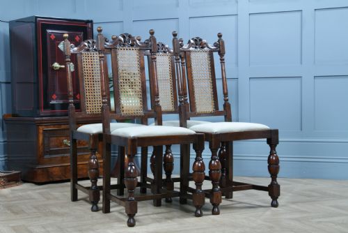 fig 4. A set of four dark oak Jacobean Revival dining chairs featuring woven cane backs, carved crests, turned legs, and cream fabric seats.
