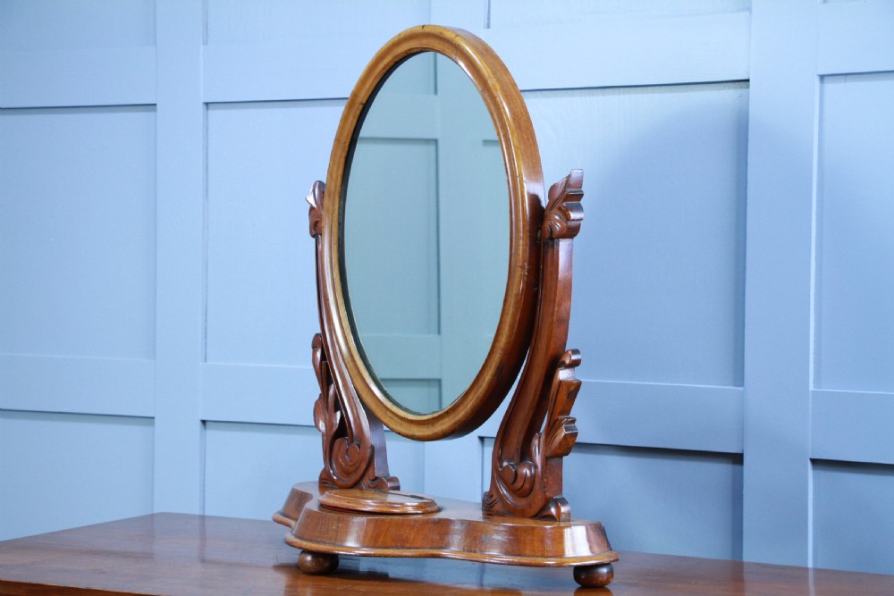 A Victorian mahogany swing toilet mirror featuring an oval moulded frame, carved scroll upright supports, and a shaped plinth base. View III