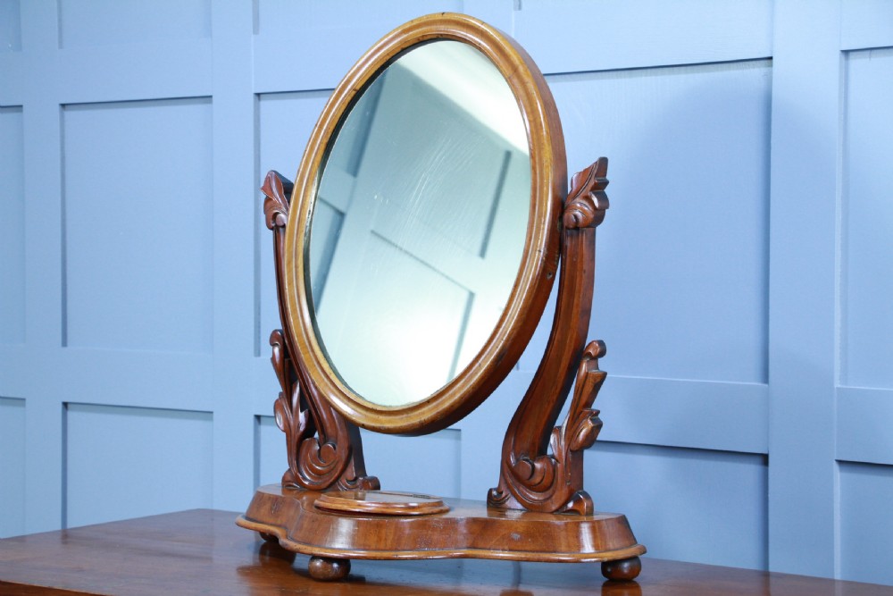 A Victorian mahogany swing toilet mirror featuring an oval moulded frame, carved scroll upright supports, and a shaped plinth base. View IV