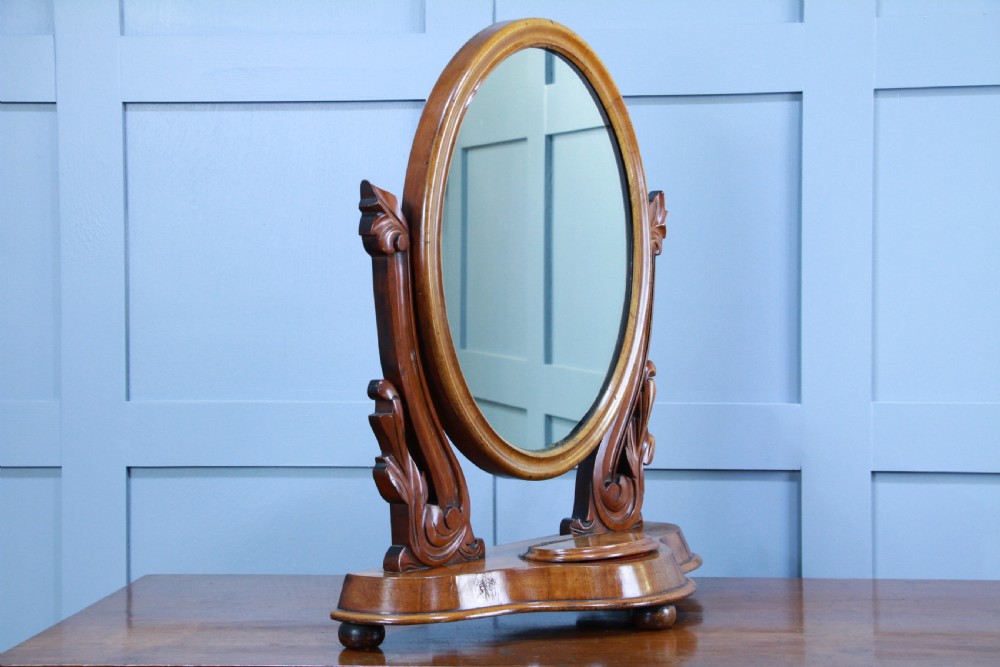 A Victorian mahogany swing toilet mirror featuring an oval moulded frame, carved scroll upright supports, and a shaped plinth base. View VII