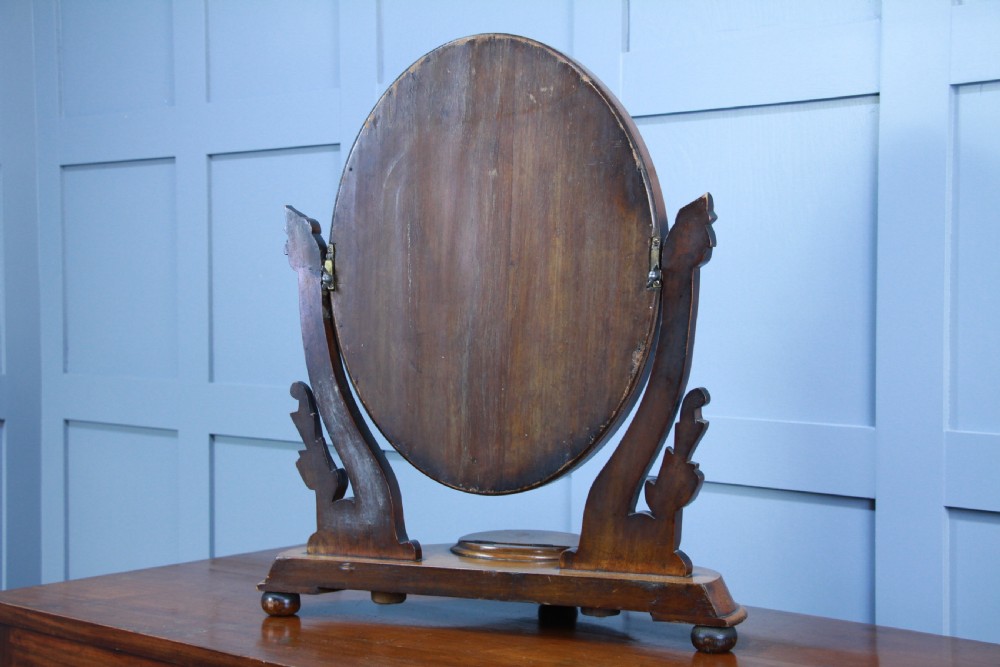 A Victorian mahogany swing toilet mirror featuring an oval moulded frame, carved scroll upright supports, and a shaped plinth base. View VIII