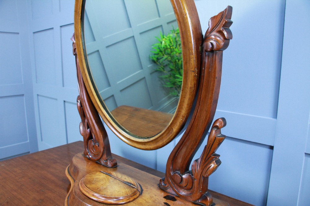 A Victorian mahogany swing toilet mirror featuring an oval moulded frame, carved scroll upright supports, and a shaped plinth base. View IX