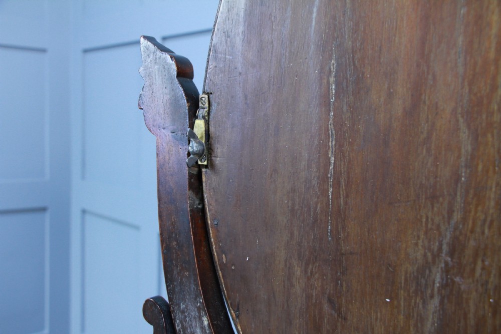 A Victorian mahogany swing toilet mirror featuring an oval moulded frame, carved scroll upright supports, and a shaped plinth base. View XI