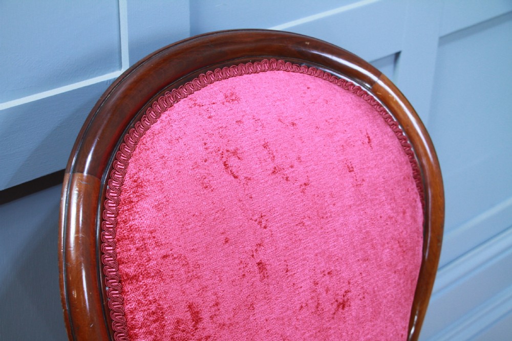 An antique Victorian balloon back nursing chair with a carved mahogany frame and deep pink velvet upholstery resting on castors. View VII
