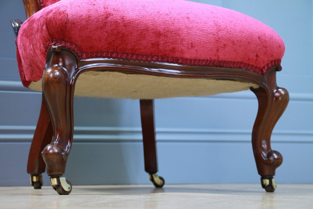 An antique Victorian balloon back nursing chair with a carved mahogany frame and deep pink velvet upholstery resting on castors. View VIII