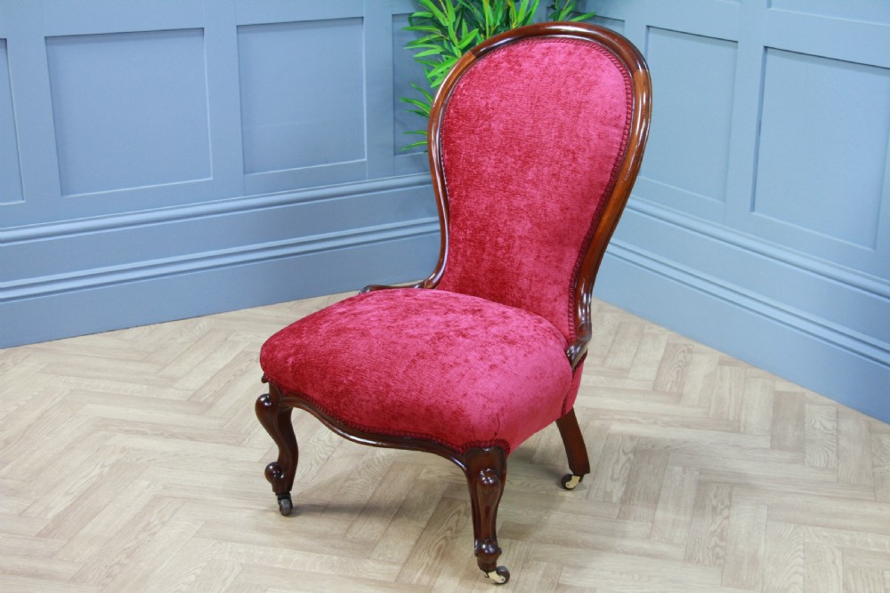 An antique Victorian balloon back nursing chair with a carved mahogany frame and deep pink velvet upholstery resting on castors. View IX